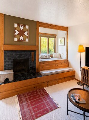Una sala acogedora con chimenea, un banco de madera y un espejo grande que refleja el exterior.