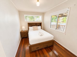 Una camera da letto con un letto di legno, un comodino, una lampada e una finestra vista su un paesaggio verde.