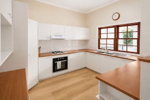 A modern kitchen with white cabinets, a wooden countertop, a stove, and a window with a view. - Southport 3BR Family Home | Free Parking & Great Location (Southport)