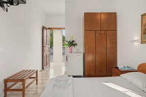 Ein Schlafzimmer mit einem Bett, einem Holzschrank, einer Bank, einem kleinen Tisch und einem Kühlschrank.