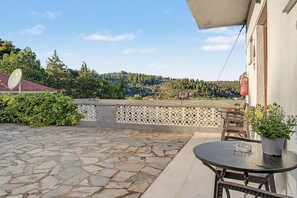 Eine terrasse mit steinbelag, einem Tisch und Stühlen, einer Satellitenschüssel und Blick auf eine hügelige Landschaft.
