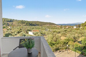 Een balkon met een tafel en een bloempot, met uitzicht op een kustdorp met huizen en begroeiing.