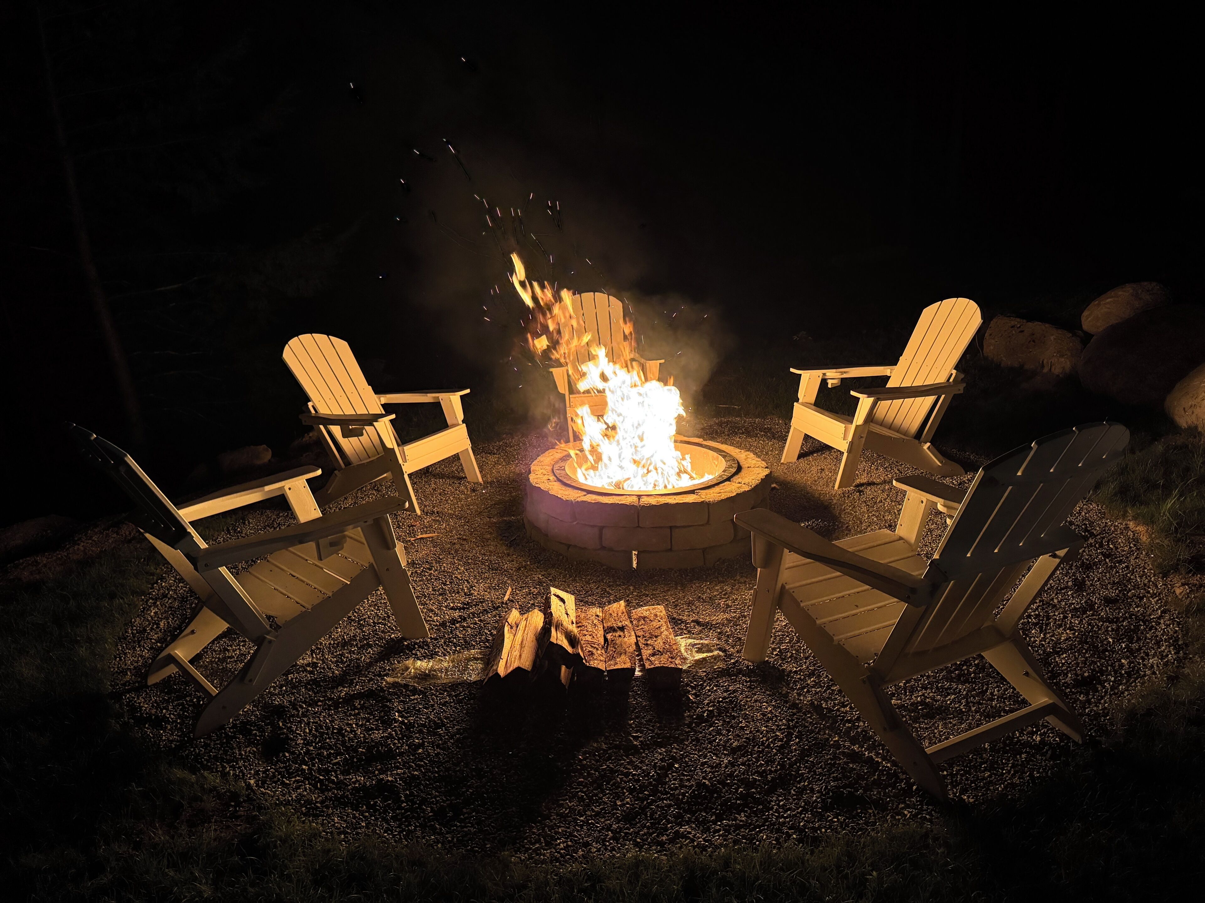 Un hogar para fuego con cuatro sillas Adirondack dispuestas alrededor.