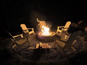 A fire pit with four Adirondack chairs arranged around it.