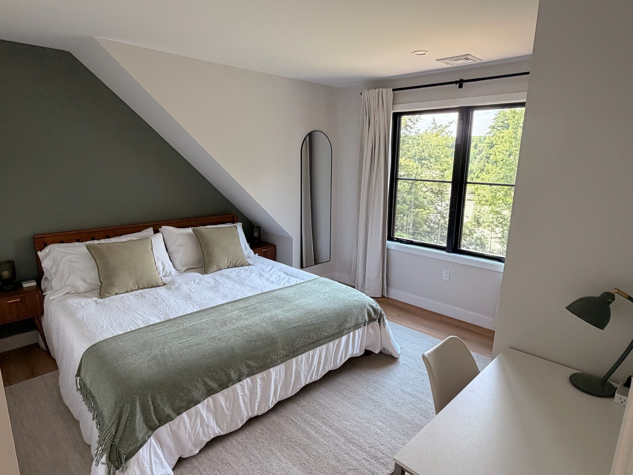 Ein Schlafzimmer mit einem Bett, einem Schreibtisch, einem Stuhl, einem Fenster und einem Spiegel.