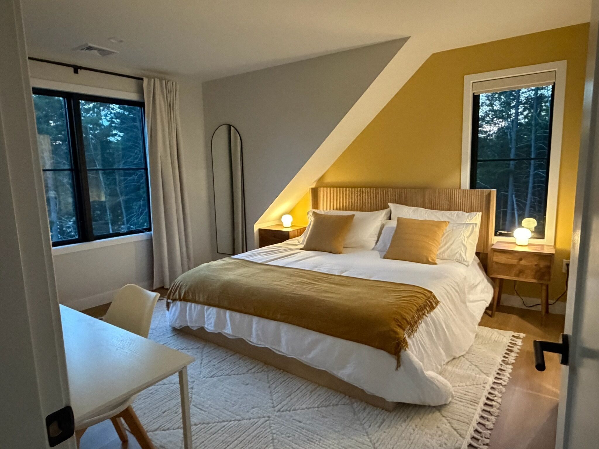 Un dormitorio con cama, mesitas de noche, escritorio y ventana.