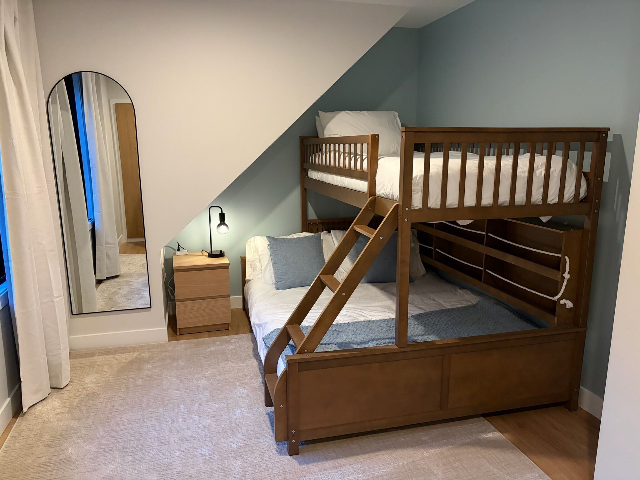 Ein Stockbett mit Schreibtisch und Stuhl, einem Spiegel und einer Lampe in einem Zimmer mit geneigten Decken.
