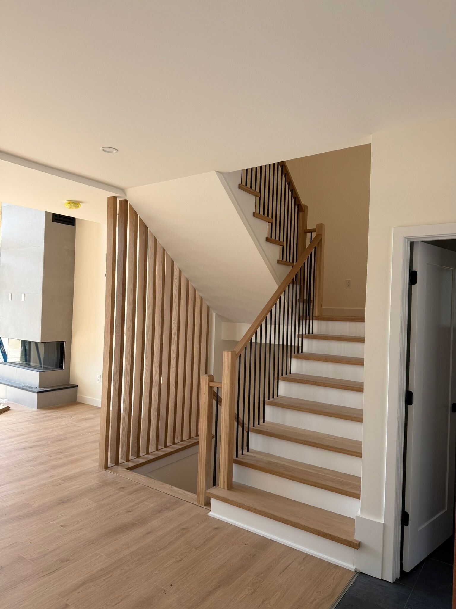A modern staircase with wooden steps and black balusters, leading to a landing.