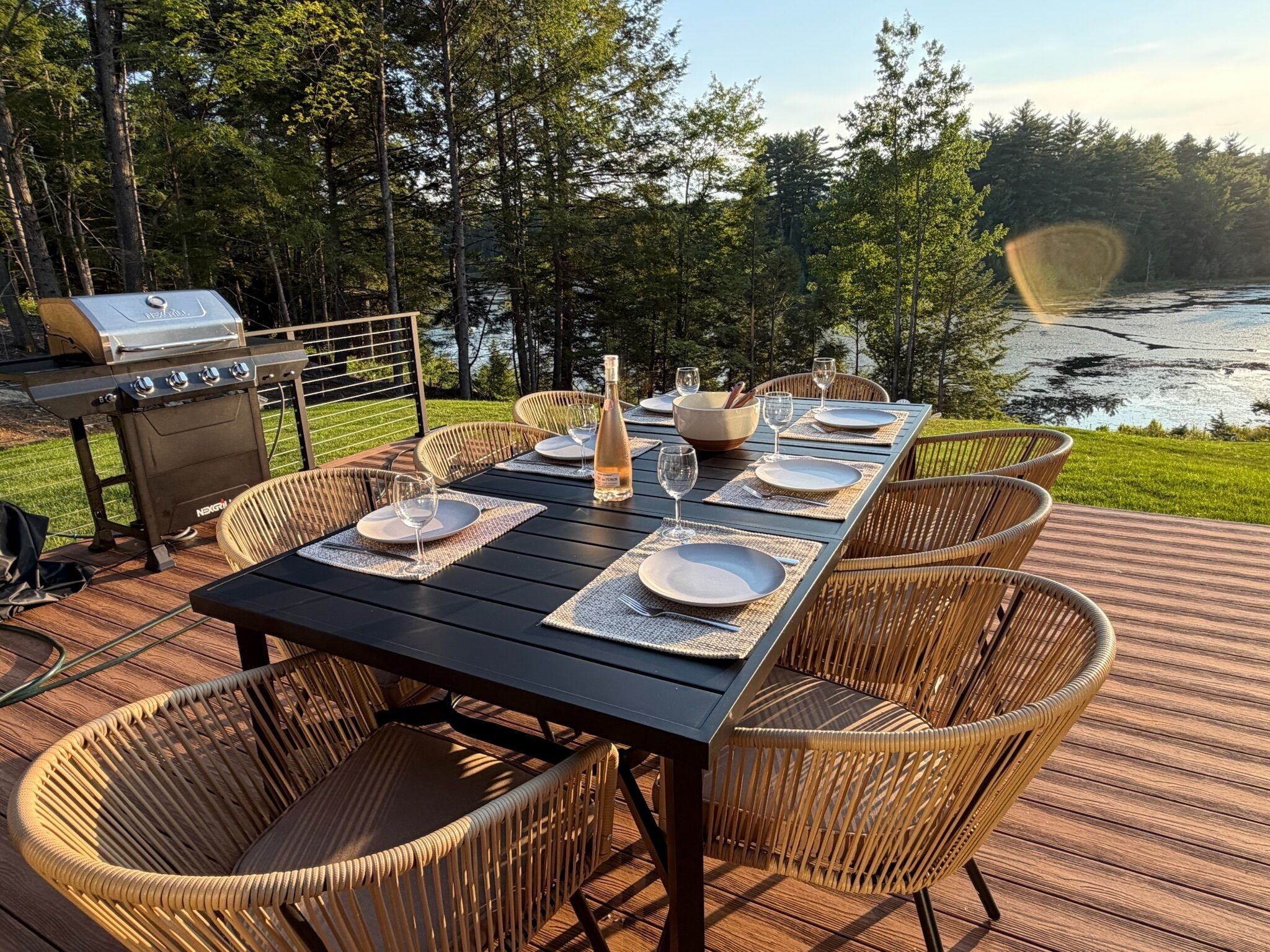 An outdoor dining area with a grill, wicker chairs, and a view of a lake.