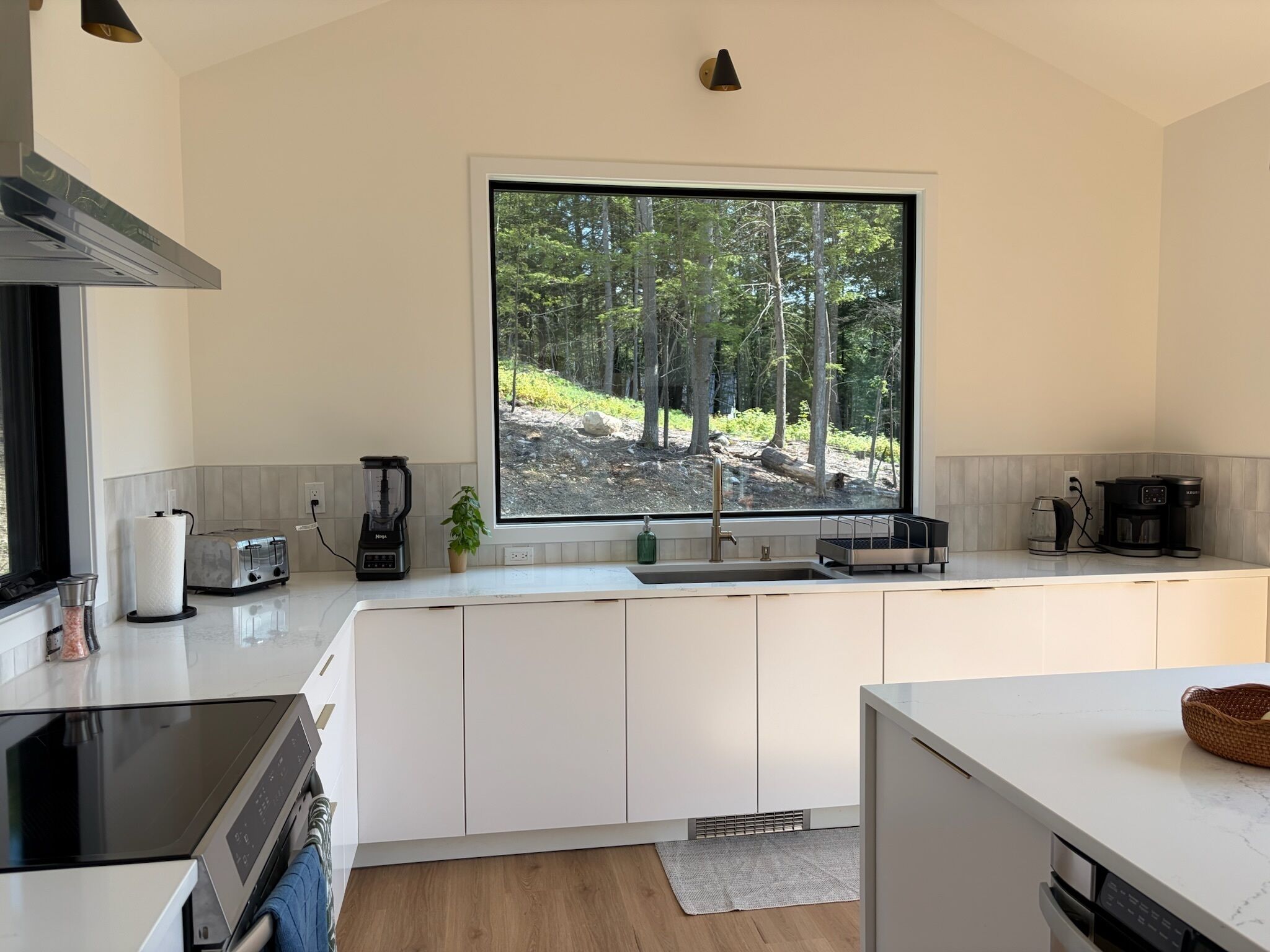 Una cocina moderna con armarios blancos, un ventanal con vistas a un bosque, un tostador empotrado y una cafetera.