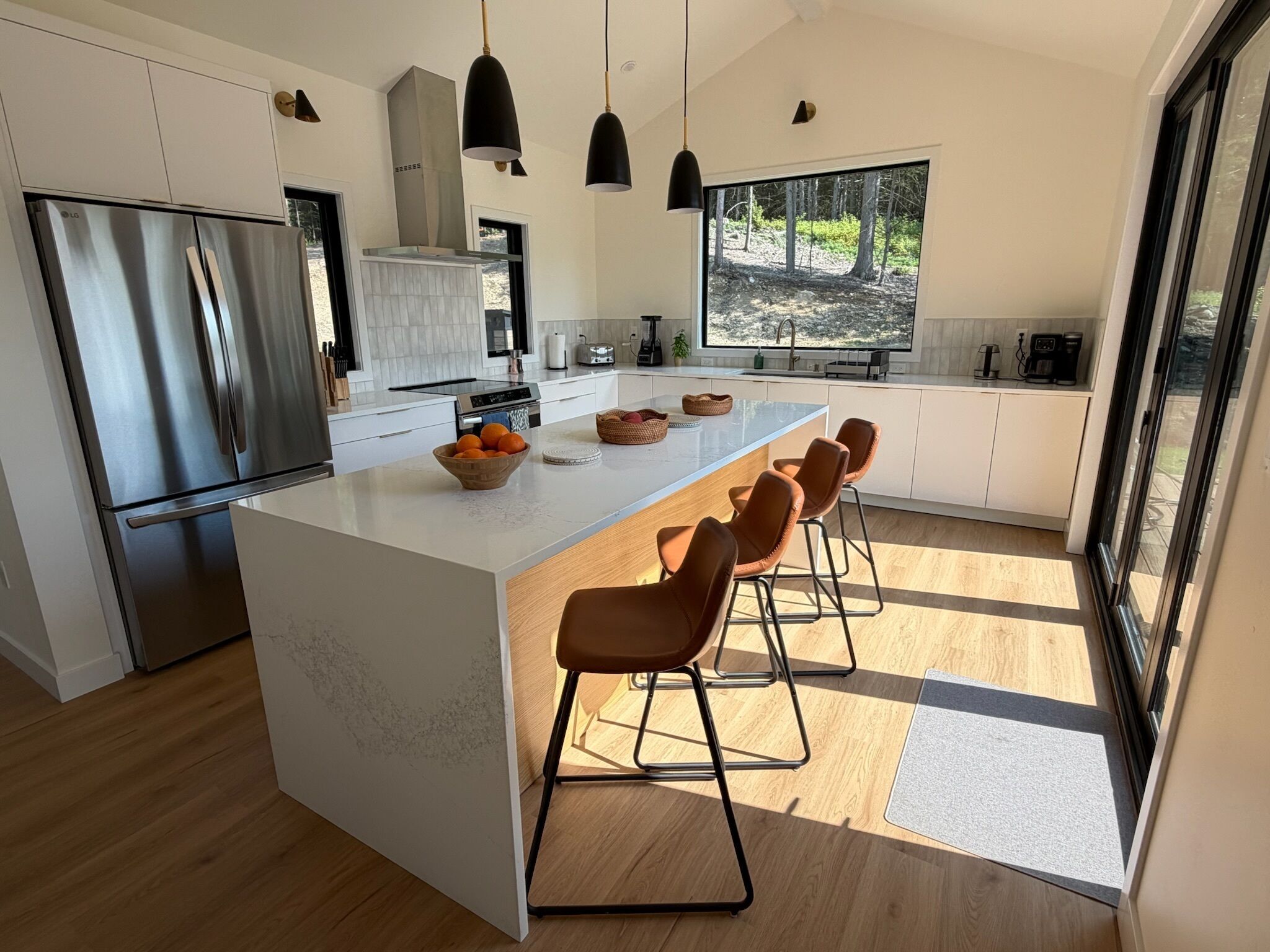 Una cocina moderna con una isla grande, electrodomésticos de acero inoxidable y vistas a un bosque desde la ventana.