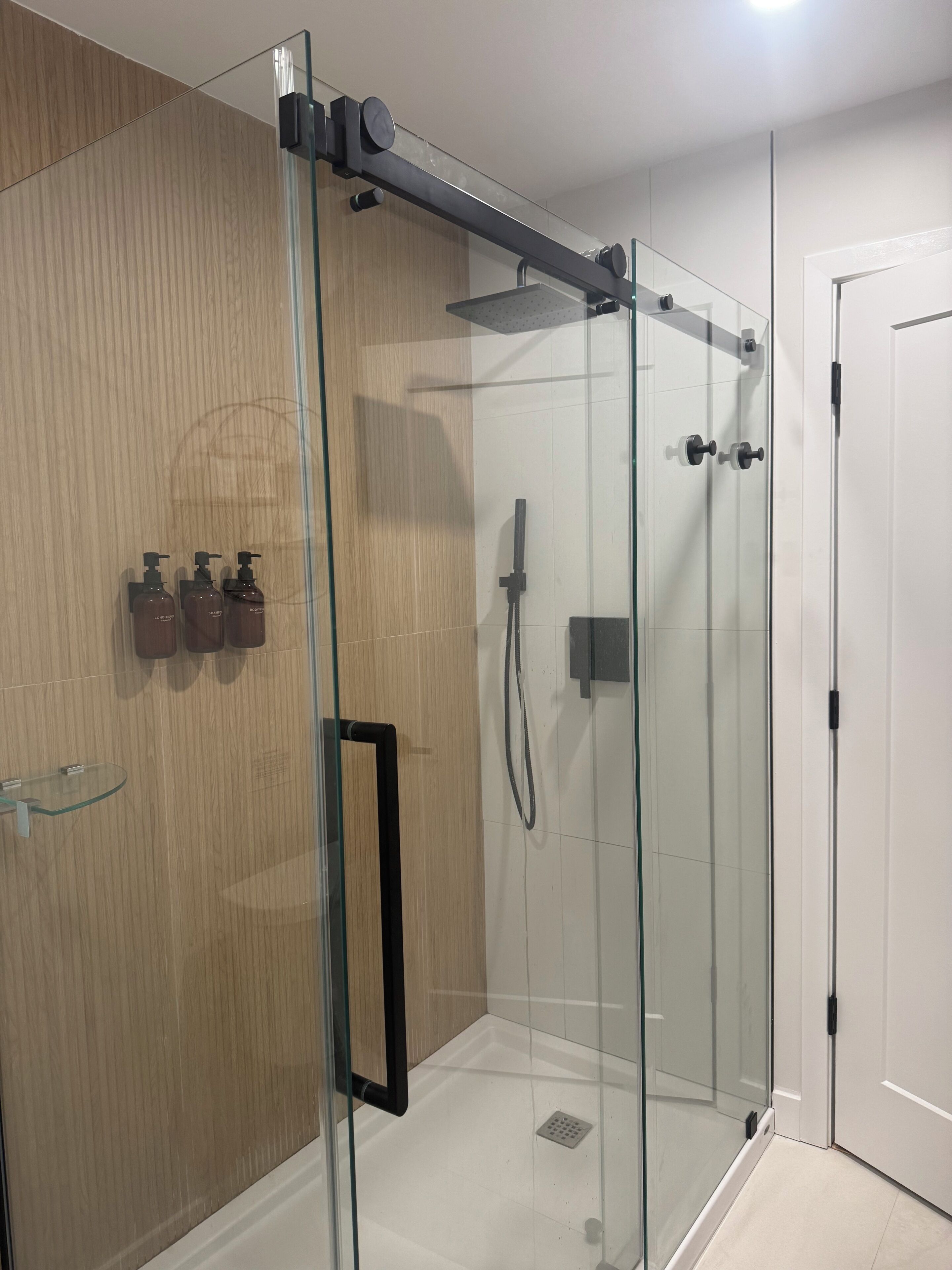 Un bagno moderno con cabina doccia in vetro, mobile lavabo in legno ed uno scaffale in vetro.