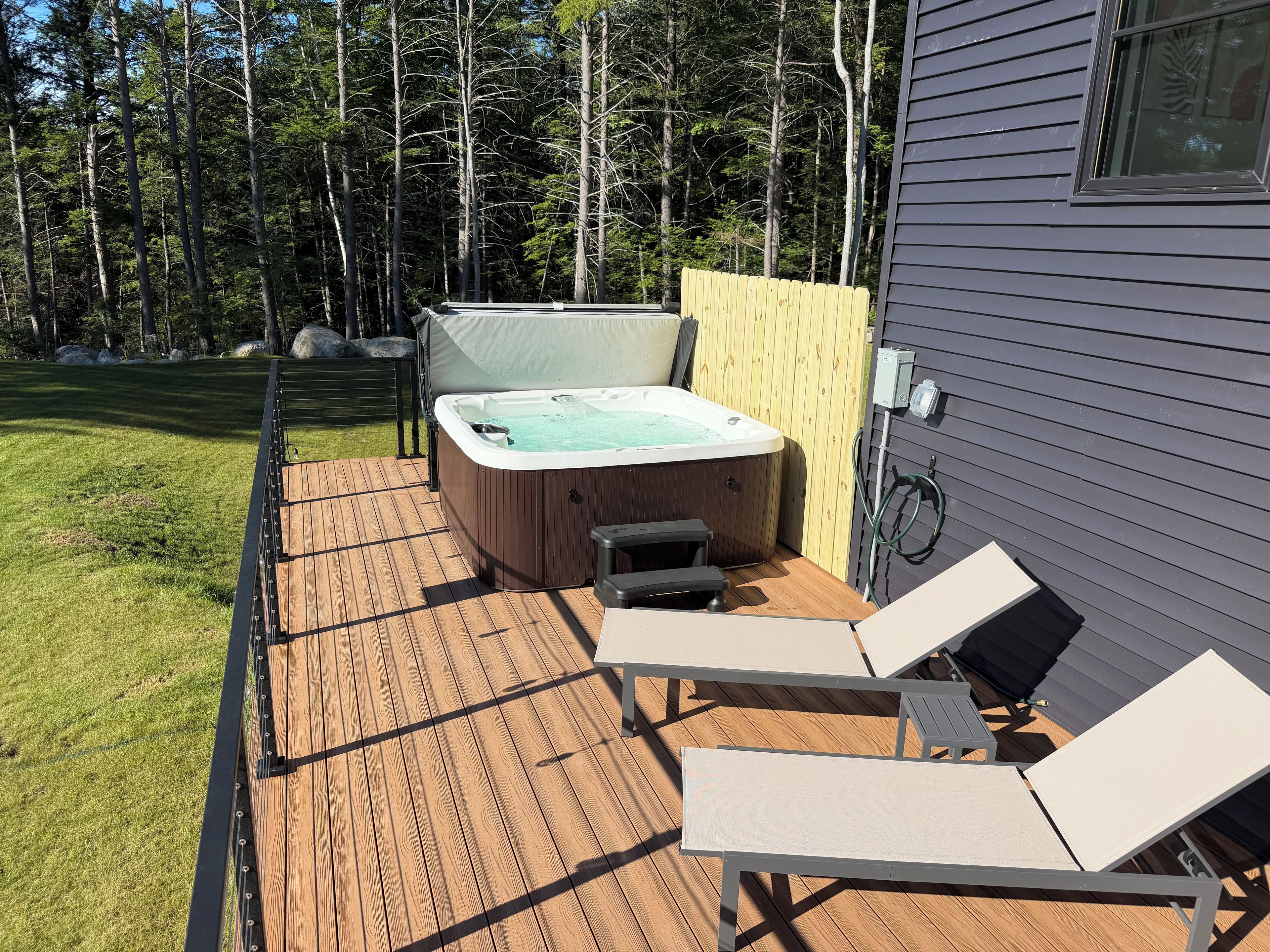 Une terrasse dotée d’un jacuzzi, de chaises longues et d’une clôture en bois.