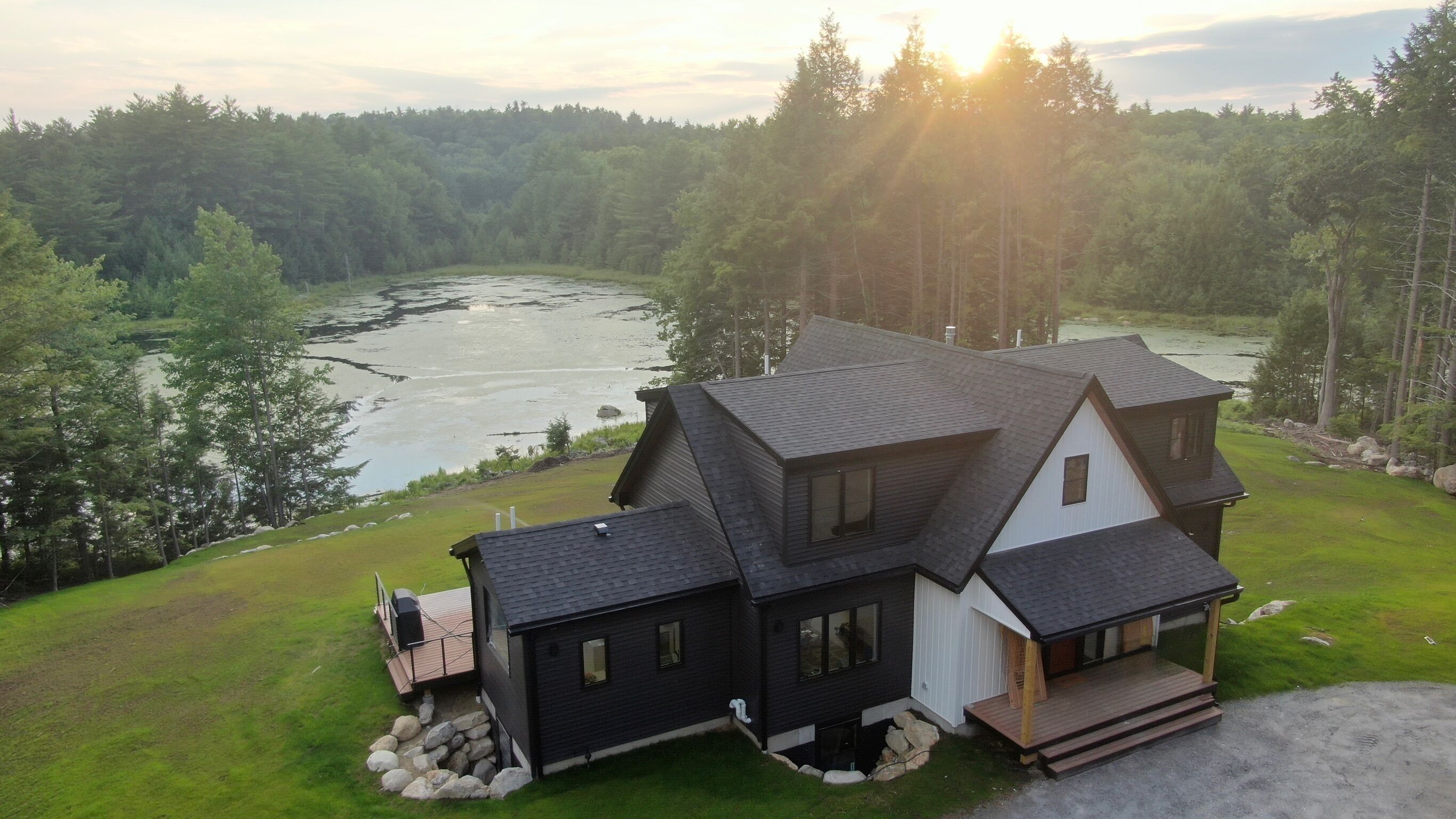 Una casa de dos pisos con un balcón, rodeada de un bosque y un río.