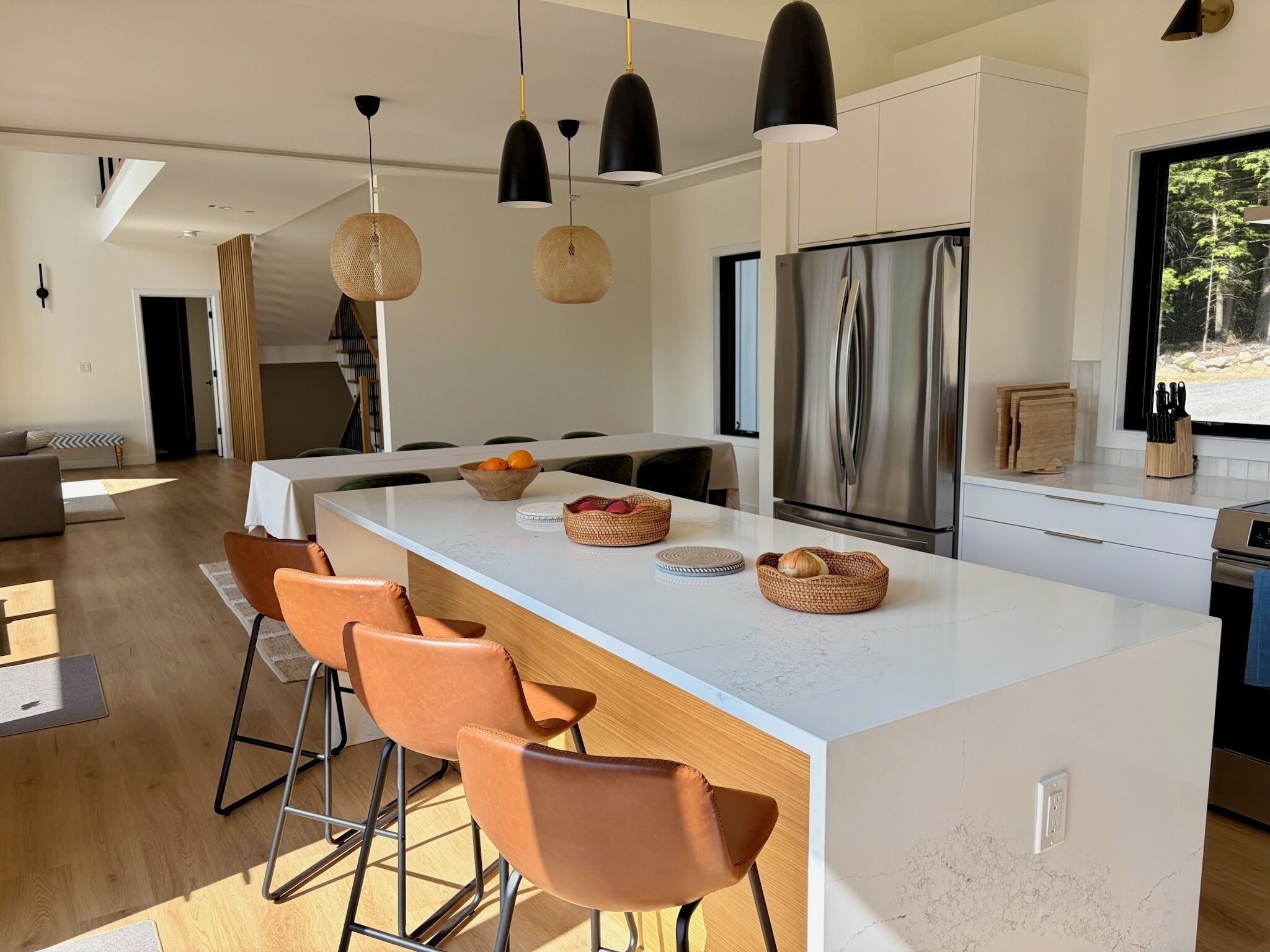 Una cucina moderna con isola centrale, sgabelli da bar, lampade a sospensione e frigorifero in acciaio inossidabile.