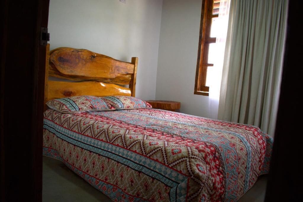 Una cama con cabecera de madera, una colcha estampada y una mesita de noche.