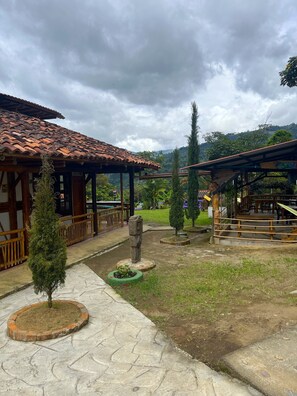 A courtyard with a tiled-roof structure, a stone statue, and a small tree.