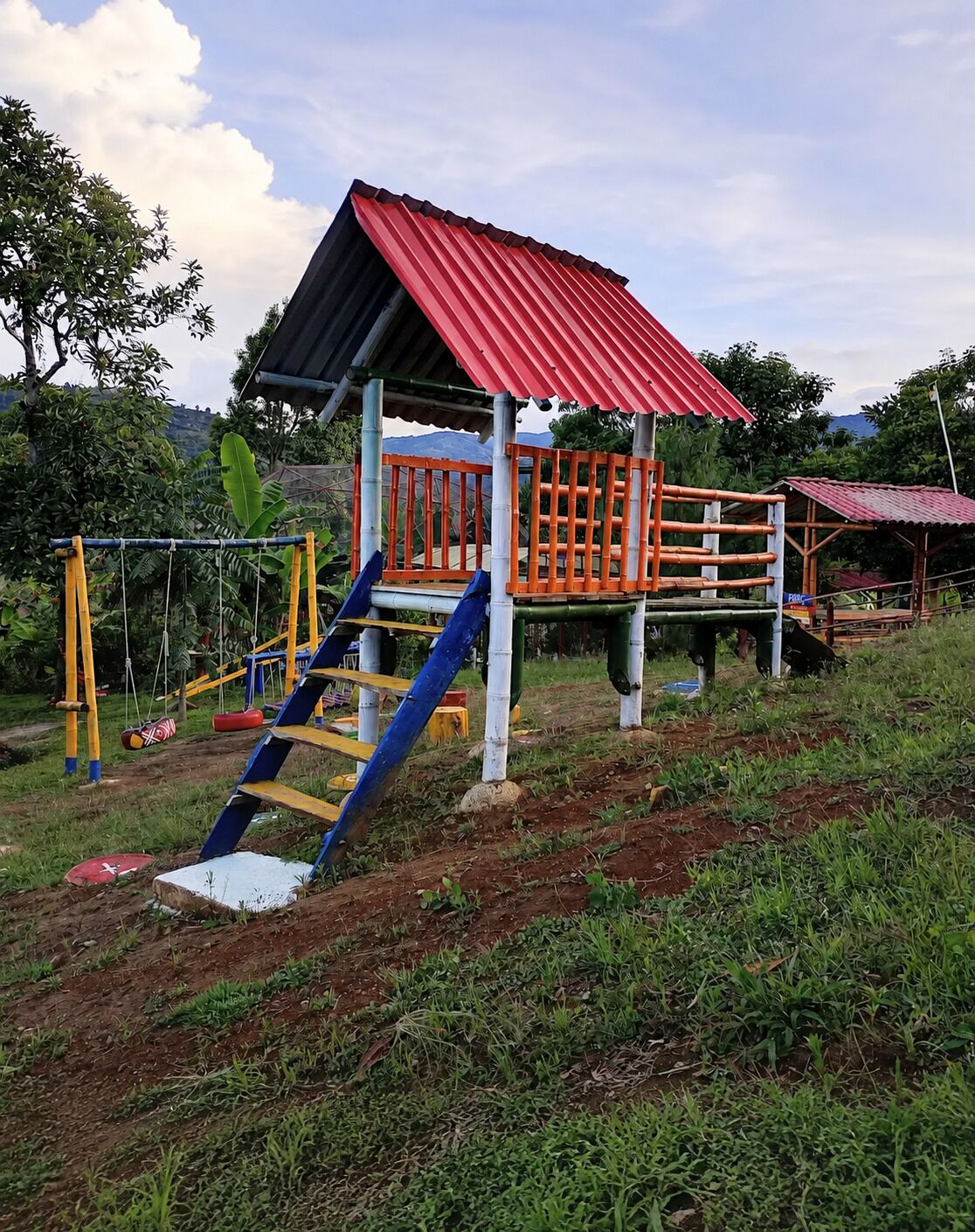 A playground with a red-roofed playhouse, a blue slide, and yellow and orange climbing structures.