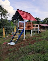 A playground with a red-roofed playhouse, a blue slide, and yellow and orange climbing structures.