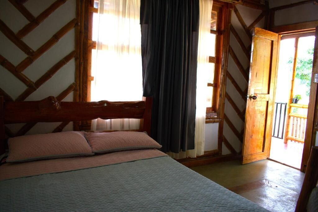 Een slaapkamer met een houten bed, een raam met gordijnen en een deur naar een buitenruimte.