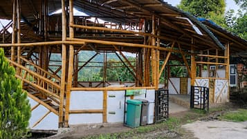 A bamboo-framed structure with a partially constructed roof, a small trash bin, and a gate.