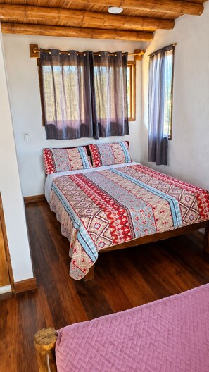 Una habitación con una cama de madera, una ventana con cortinas y piso de madera.