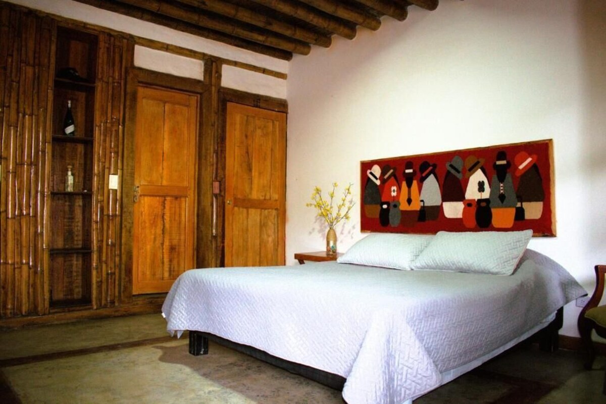 A bedroom with a large bed, wooden wardrobe, and a wall-mounted painting.
