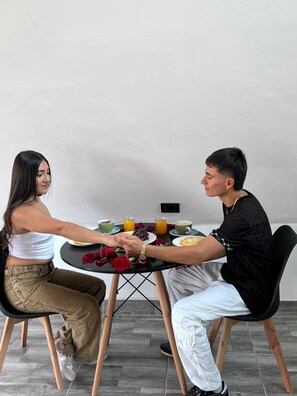 Dos personas sentadas en una mesa redonda con comida, que incluye frutas y bebidas.