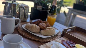 Ein Frühstückstisch mit Kaffeekanne, Croissants, einer Saftflasche und einem Teller mit Speisen.