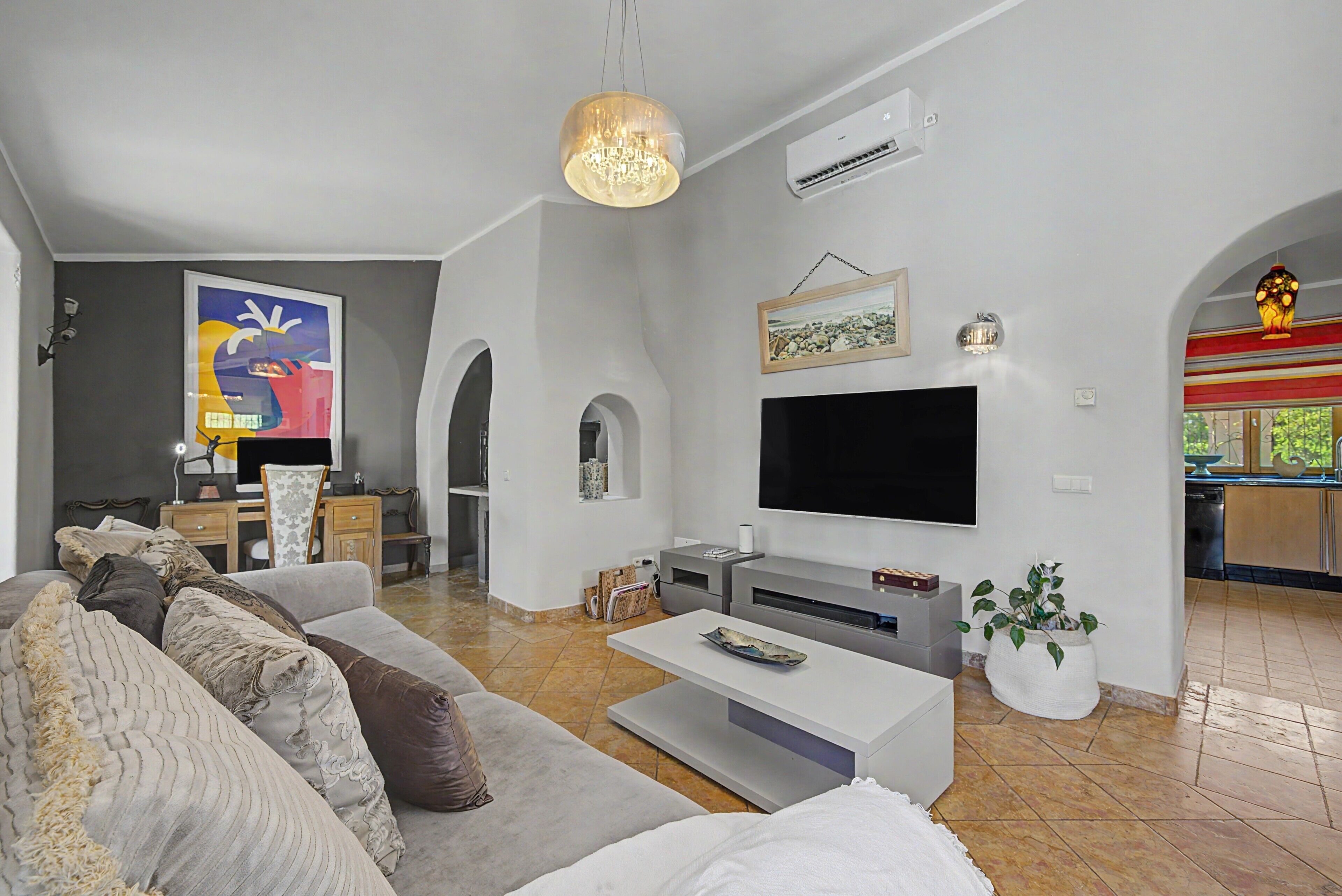 A modern living room with a large flat-screen TV, a grey sofa, and a coffee table.