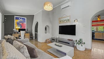A modern living room with a large flat-screen TV, a grey sofa, and a coffee table.