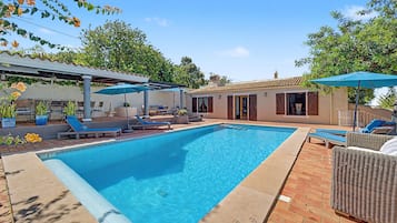 A rectangular swimming pool with a tiled edge, surrounded by lounge chairs and umbrellas.