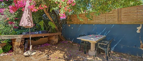 A patio area with a table and chairs, surrounded by a wooden fence and a garden with pink flowers.