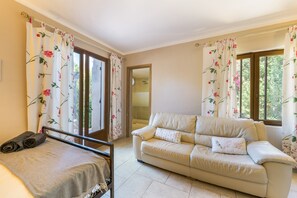 A room with a bed, a sofa, and a window with floral curtains. - Room 'Pool House' with Shared Pool, Wi-Fi and Air Conditioning (Almancil)