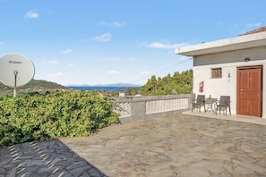 A stone-paved outdoor area with a satellite dish, a table with chairs, and a view of the sea and hills. - Room 'Orama  13' with Shared Terrace, Wi-Fi and Air Conditioning (Εύβοια)