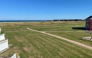 Een gazon met een duidelijk pad naar een strand, een rood gebouw en een witte omheining.