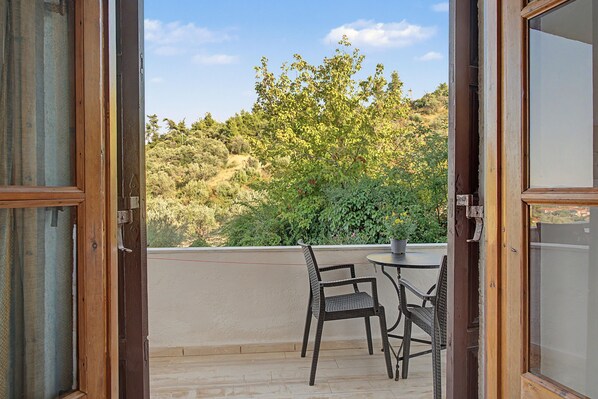 Ein offener Balkon mit Tisch und Stühlen, der einen Blick auf einen Hügel mit Bäumen und Sträuchern bietet.