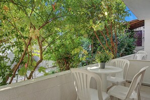 An outdoor seating area with white plastic chairs and a table, surrounded by lush green foliage and a clear blue sky. - Room 'Orama 24' with Sea View, Wi-Fi and Air Conditioning (Εύβοια)