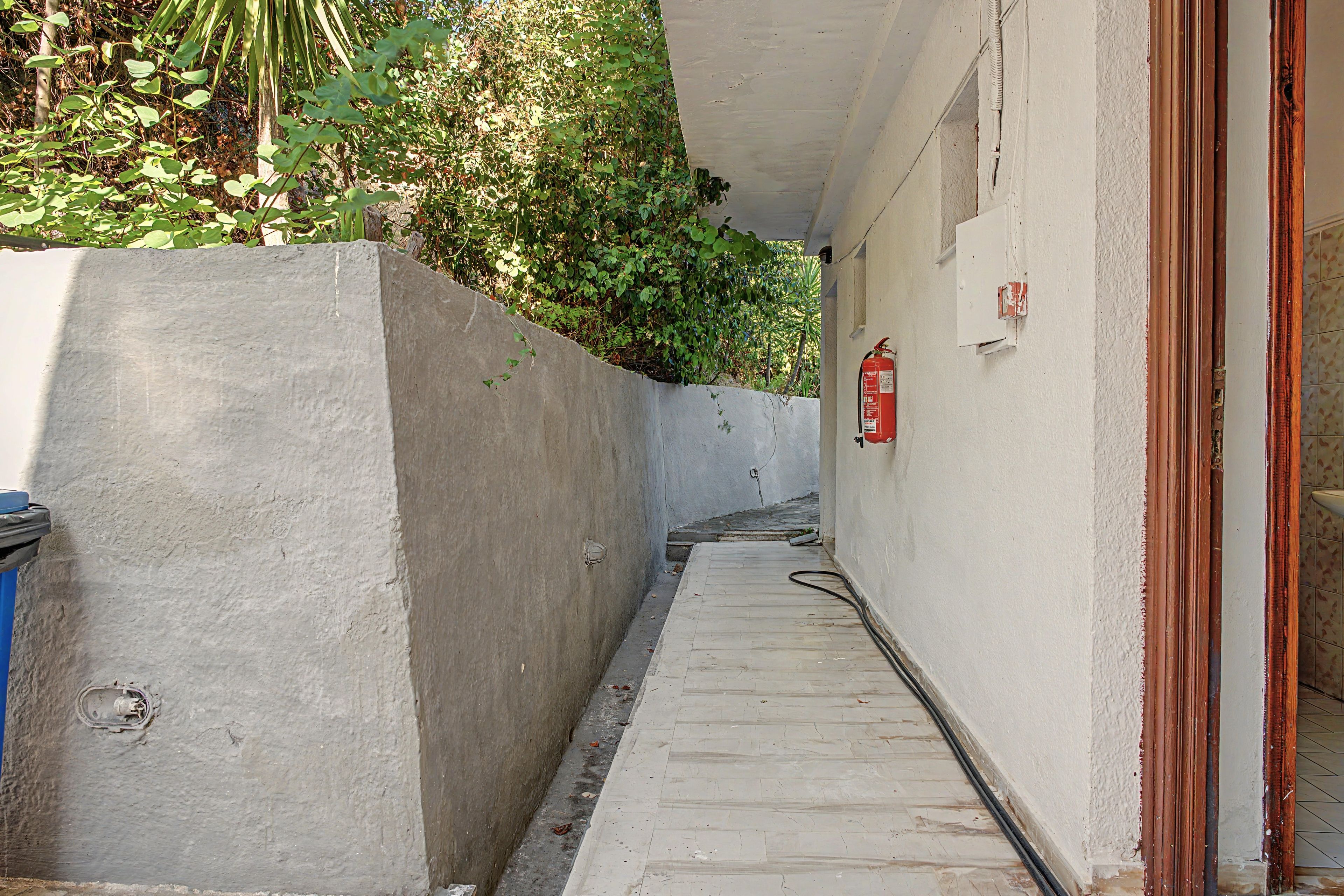 Un estrecho sendero de concreto que lleva a la entrada de un edificio, con un extintor de incendios sujeto a la pared.