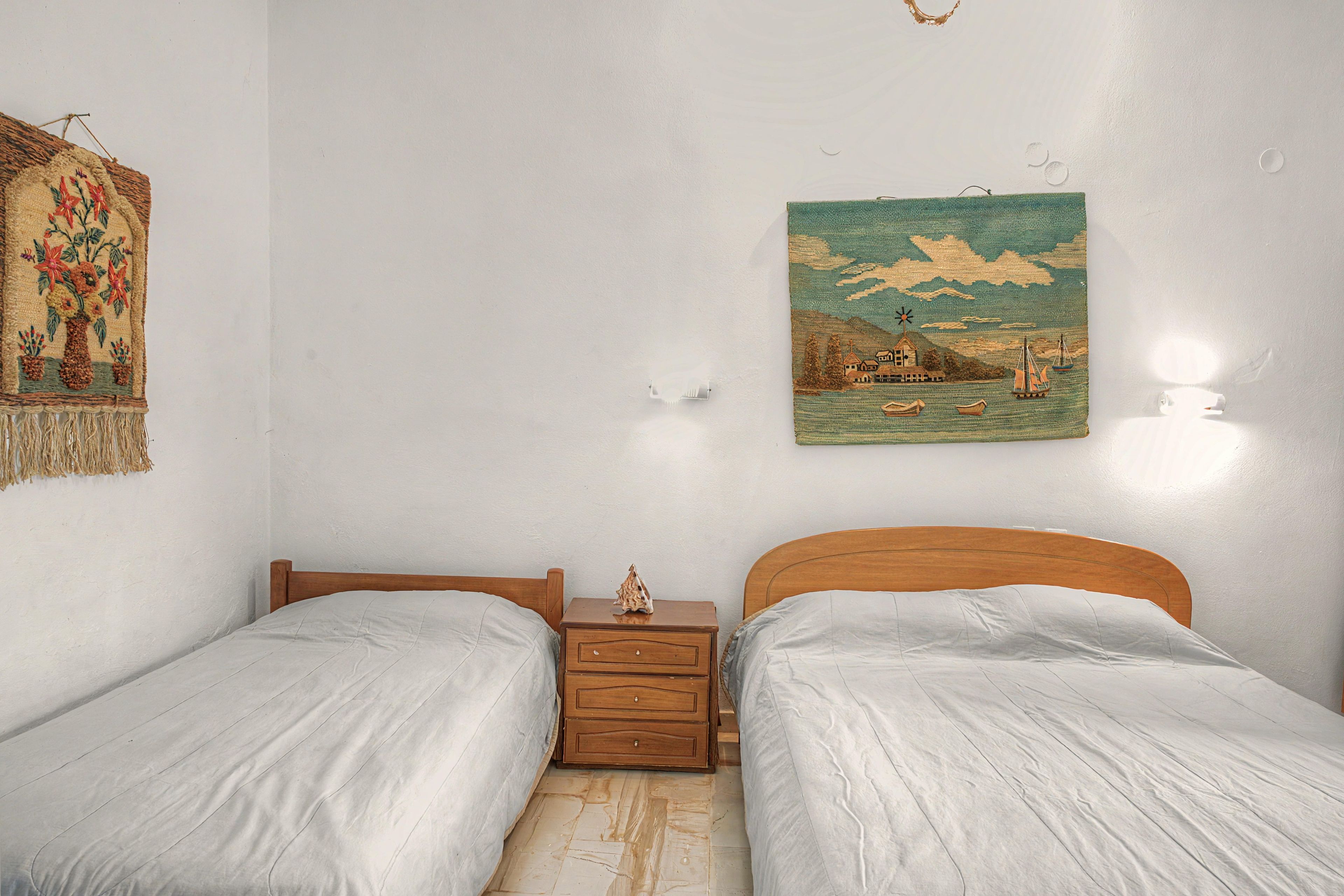 Ein Zimmer mit zwei Einzelbetten, einem Nachttisch mit Lampe, einer Wanddekoration und einem Gemälde.