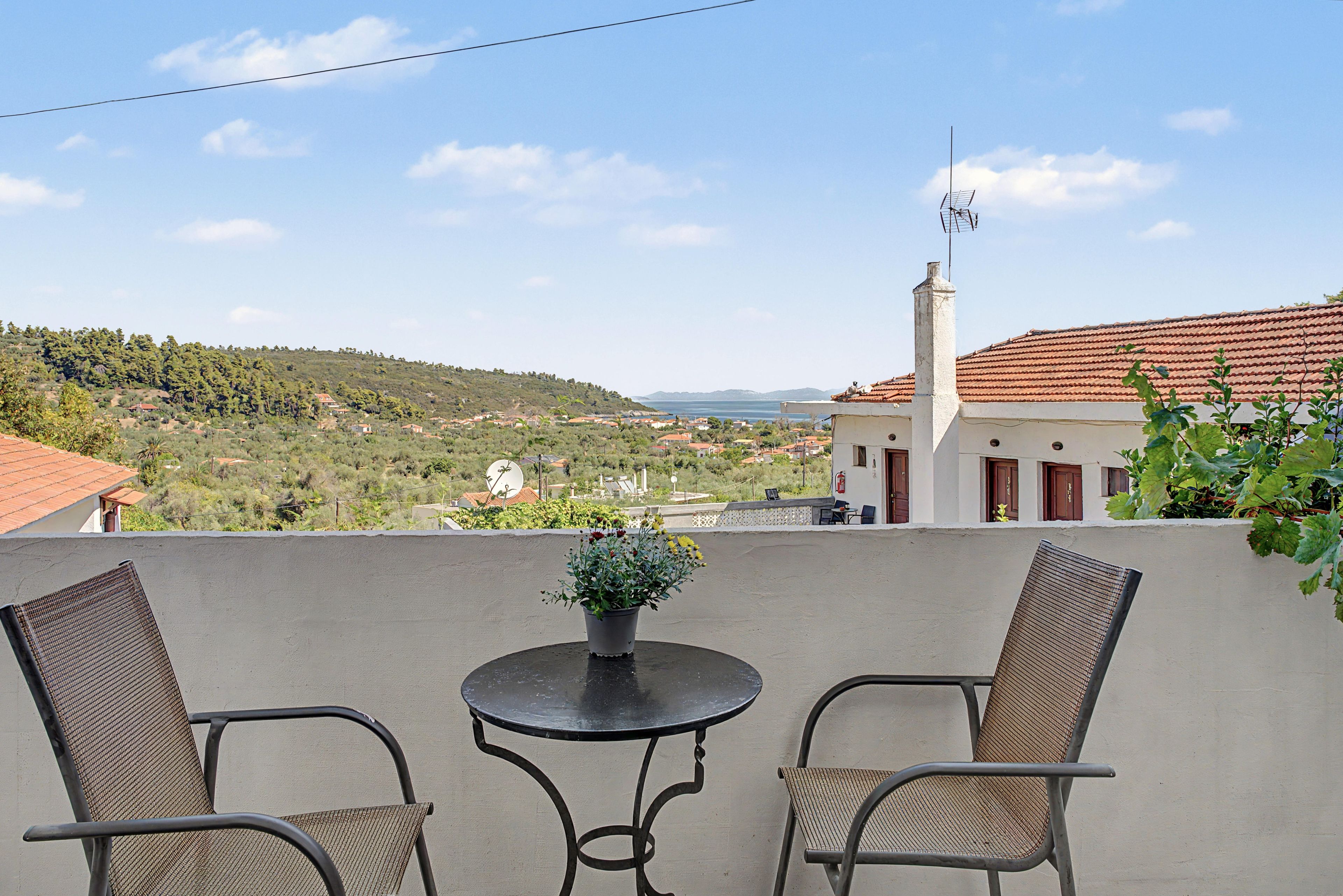 Un balcón con dos sillas y una mesa, con vistas a un paisaje costero con casas y vegetación.
