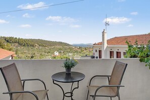 Un balcon avec deux chaises et une table, donnant sur un paysage côtier avec des maisons et de la végétation.