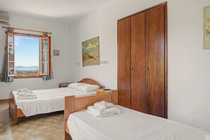 Ein Schlafzimmer mit zwei Betten, einem Holzschrank, einem Fenster mit Vorhängen und einem Gemälde an der Wand.