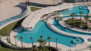 Ein Resort mit großem Poolbereich, Palmen und einer Promenade direkt am Strand.