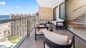 Ein Balkon mit Blick auf einen Strand und ein Hochhaus, ausgestattet mit zwei Stühlen und einem kleinen Tisch.