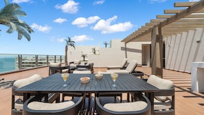 Una terraza exterior con una mesa de madera, sillas y vista al océano.