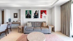 A modern living room with a grey sofa, two patterned throw pillows, a round coffee table, and a desk with a computer and a framed picture. - One 1702 Penthouse: Star Wars Luxury Penthouse (Puerto Peñasco)