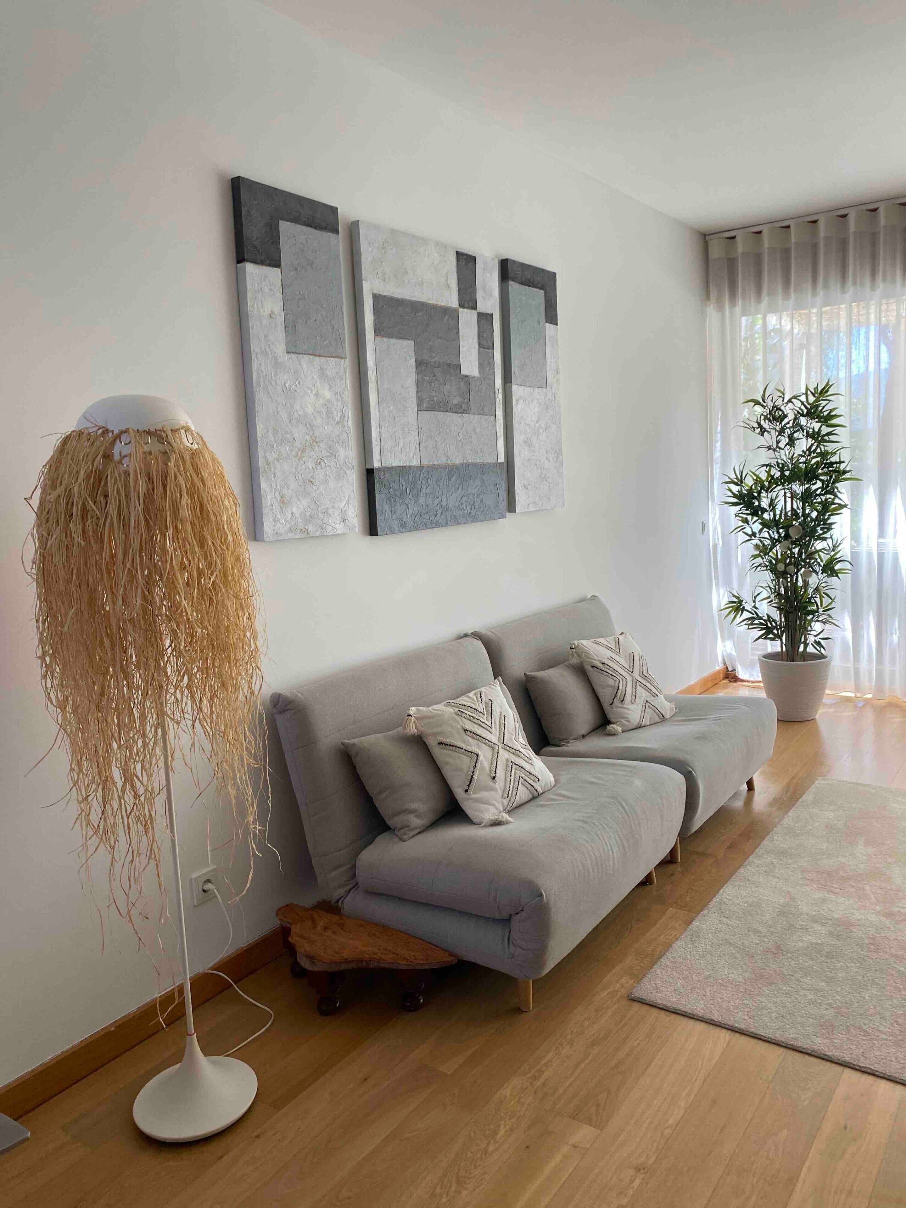 Een moderne woonkamer met een grijze bank, een vloerlamp en abstracte muurkunst.