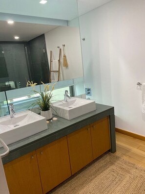 Un baño con lavamanos doble, un espejo grande y un perchero para toallas.