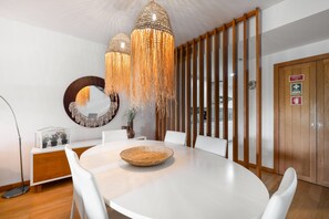 Een moderne eetruimte met een ronde tafel, witte stoelen, een geweven decoratiestuk en een hanglamp.